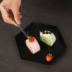 Stainless steel plating tongs placing dessert on a black plate