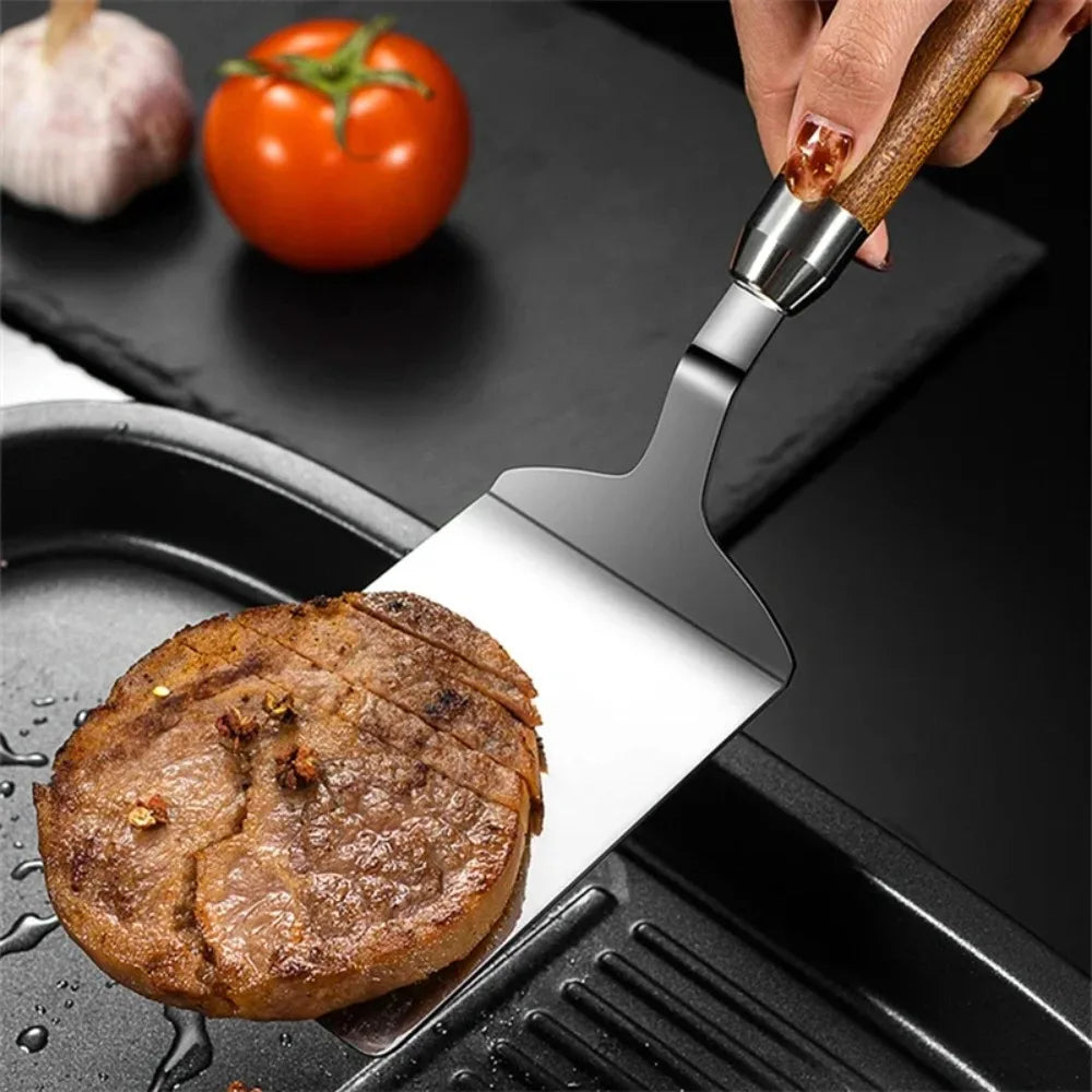 Stainless steel griddle spatula lifting a steak from a grill pan