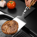 Stainless steel griddle spatula lifting a steak from a grill pan