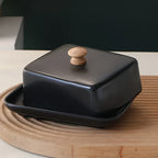 Black ceramic butter dish on a wooden board